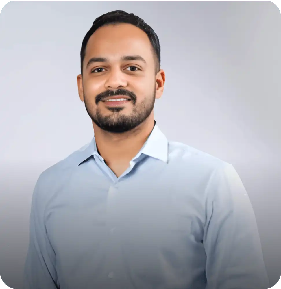 Smiling man in a light blue shirt posing against a plain background in a professional headshot.