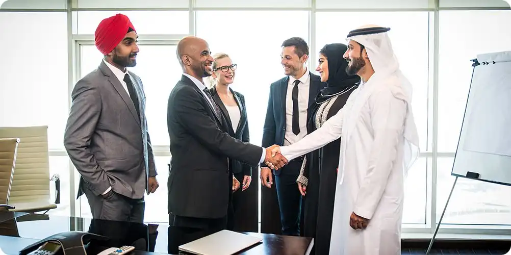 Strategic alliances image featuring four diverse professionals gathered around a table discussing contracts and shaking hands.