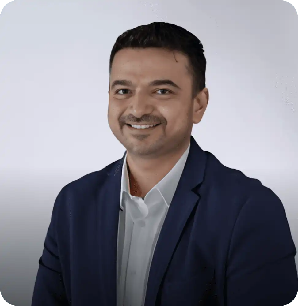 Smiling man in a navy blue suit and white shirt, posing against a light background in a professional portrait.