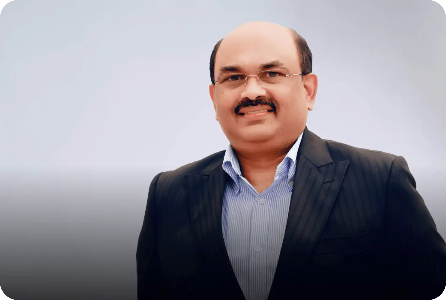 Professional portrait of a middle-aged man in a dark suit and striped shirt, smiling against a light background.