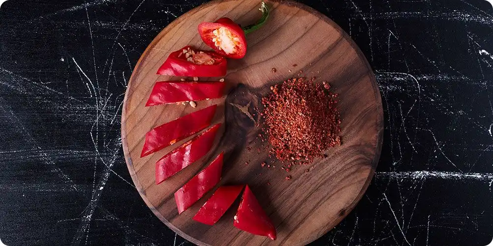 A close-up photo of dried red paprika pods and a pile of its deep red powder, used to provide natural red color to food.