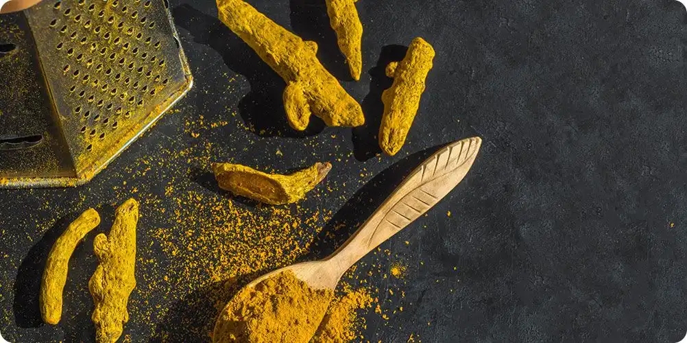 A close-up of whole and ground turmeric rhizomes, showcasing its rich, golden-yellow color for natural food applications.